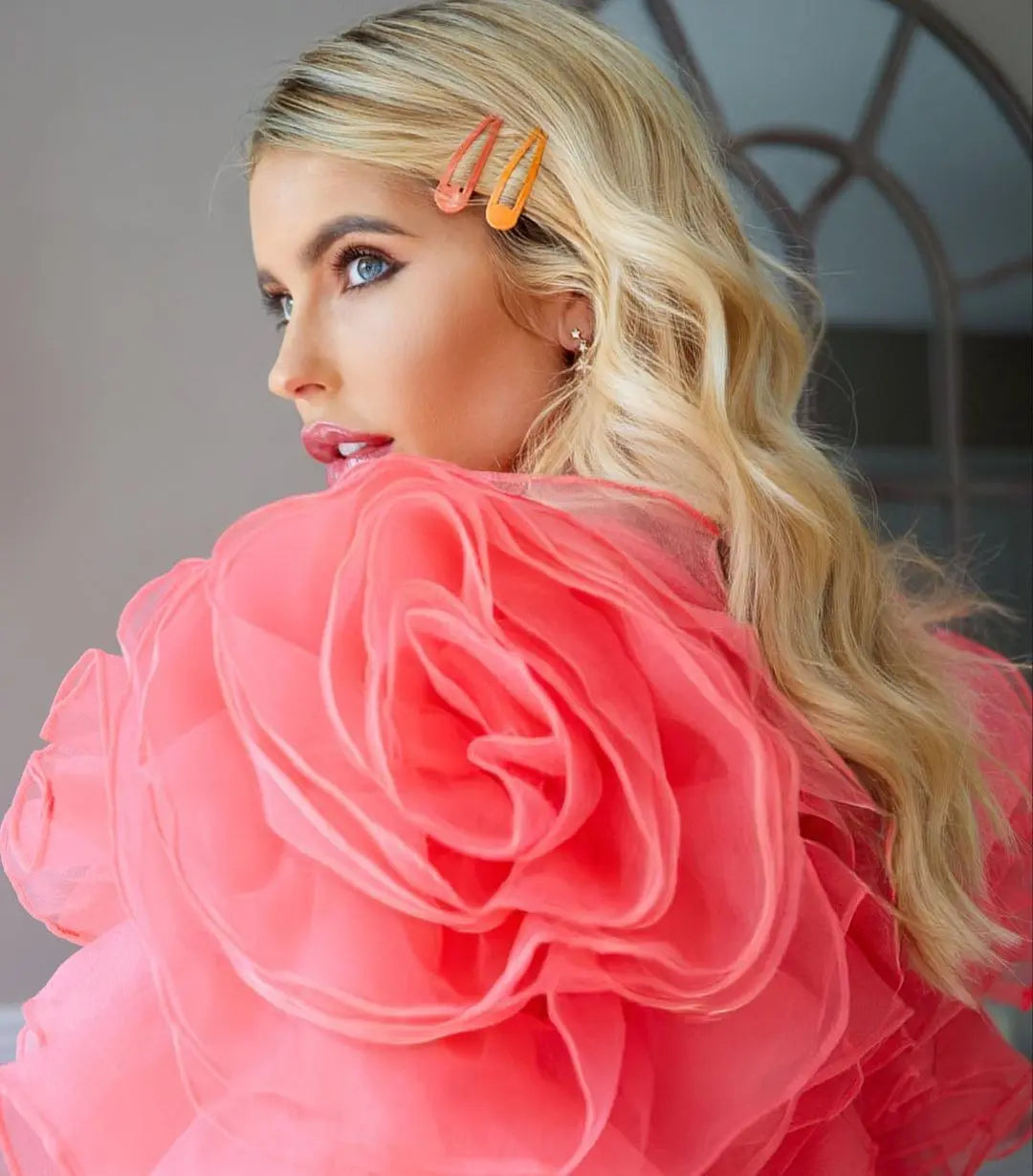 A blonde woman in a pink dress and flower hair clip, showcasing glamorous waves for a chic and romantic look at Royal Ascot.